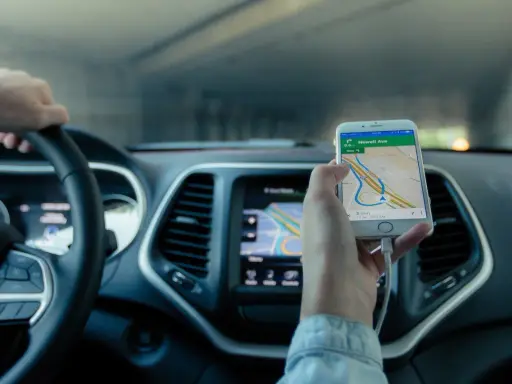 Mano al volante, móvil con mapa GPS mostrando cómo funciona un localizador GPS para coche.