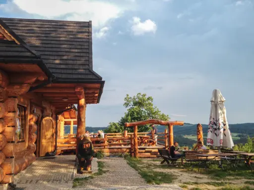 Drewniana bacówka Jamna z tarasem, gdzie goście jedzą, a obok stoi parasol. Menu bacówki Jamna kusi widokiem.