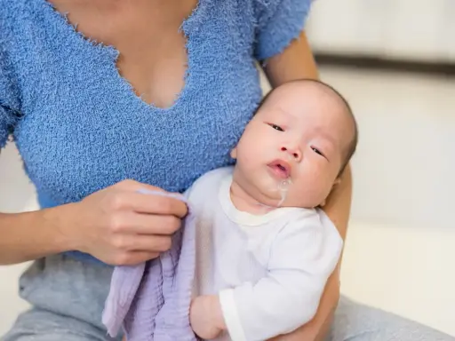 Un neonato con rigurgito, tenuto in braccio dalla madre che ha un panno viola.