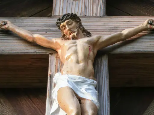 Jesus gekreuzigt, mit Dornenkrone und Wunden, hängt an einem Holzkreuz.