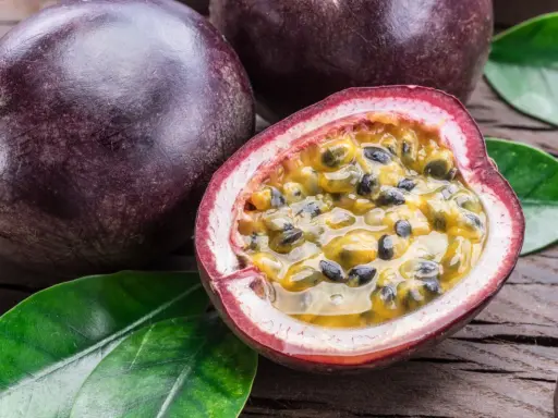 Dunkle, runde Früchte liegen auf Holz. Eine davon ist aufgeschnitten und zeigt das saftige Fruchtfleisch mit Kernen – eine köstliche Passionsfrucht Maracuja.