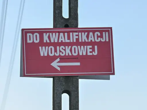 Czerwony znak z białym napisem "DO KWALIFIKACJI WOJSKOWEJ" i strzałką w lewo. Kategoria: d wojsko.