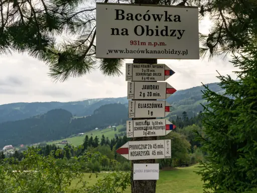 Tablica z drogowskazami na szlak na Radziejową. W tle górzysty krajobraz Beskidu Sądeckiego.