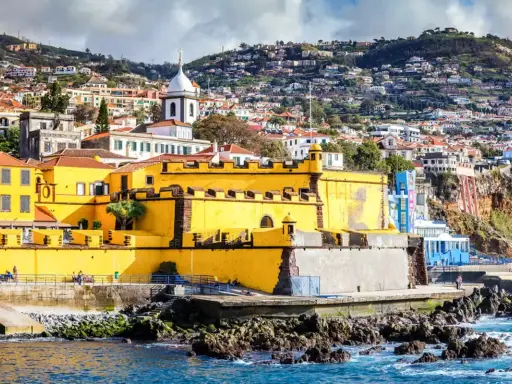Gelbe Festung in Funchal, Madeira, mit Häusern, die sich den Hang hinaufziehen.