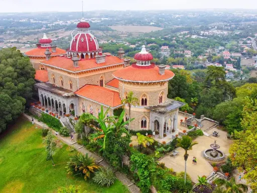 Der Monserrate Palast thront auf einem Hügel, umgeben von üppiger Vegetation und einer malerischen Stadt. Seine roten Dächer und Türmchen sind ein Blickfang.
