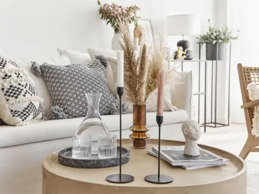 Un accogliente salotto bohemien con cuscini decorativi, un vaso di erba della pampa e candele su un tavolino rotondo.