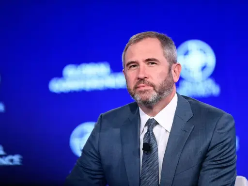 Brad Garlinghouse, CEO Ripple, w niebieskim garniturze, z brodą, na tle niebieskiej sceny z logo Global Conference.