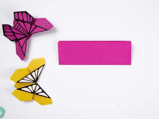 Zwei bunte origami schmetterlinge, einer pink mit Punkten, der andere gelb mit Punkten und Flügelmustern, liegen neben einem Streifen pinken Papiers.