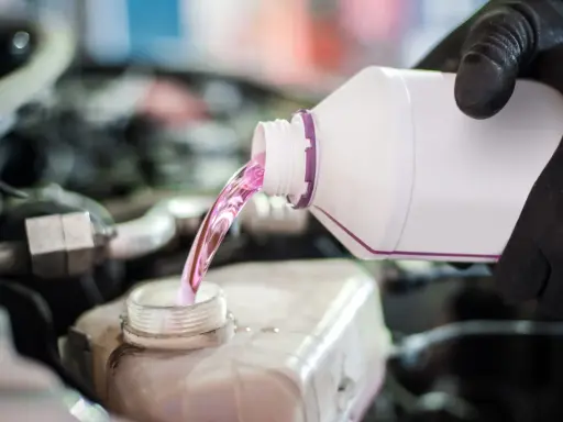Mano con guante negro vierte líquido rosa, agua de motor coche, en depósito.