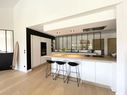 Cuisine moderne avec îlot central, plan de travail en bois et verrière industrielle. Une belle idée cuisine avec verriere pour un espace lumineux.