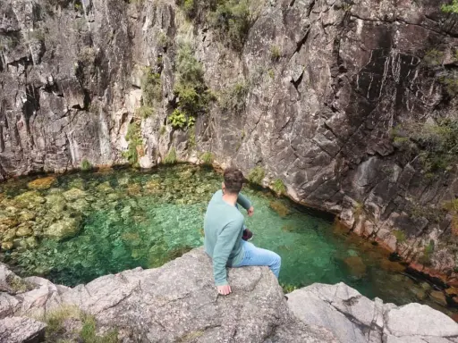 Mann sitzt auf Felsen am kristallklaren Wasser des Peneda-Gerês-Nationalparks.
