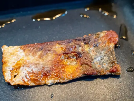 Ein Stück Lachs braten in der Pfanne, die Haut ist knusprig und goldbraun, das Fleisch saftig.