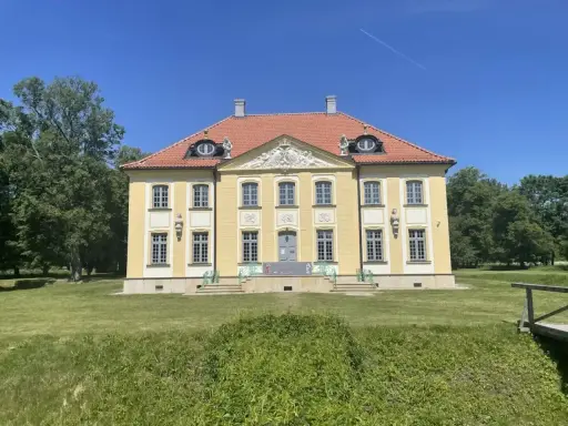 Piękny, żółty pałac w Choroszczy z czerwonym dachem, otoczony zielenią i błękitnym niebem.