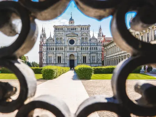 La Certosa di Pavia, un capolavoro rinascimentale, vista attraverso un cancello decorato. Un percorso conduce alla maestosa facciata.