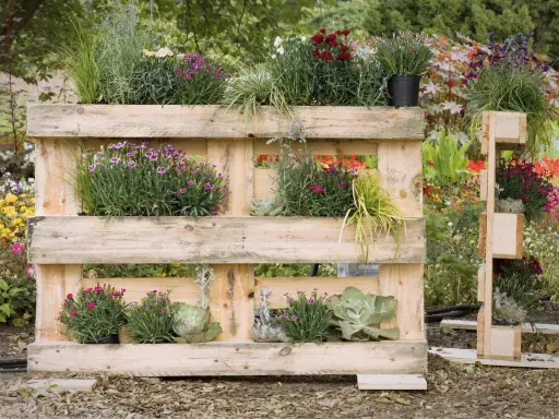 Jardinière en palette accueillant des fleurs roses et violettes, des graminées et des succulentes. Un jardin vertical original et écologique.