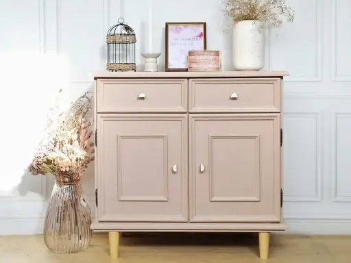 Meuble en bois peint en rose poudré, avec deux tiroirs et deux portes. Décoration florale et cage ornementale sur le dessus.