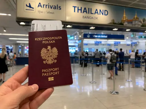 Polski paszport i bilet lotniczy w ręku, w tle tablica "THAILAND BANGKOK" i stanowiska "Visa on Arrival". Sprawdzanie tajlandia warunki wjazdu.