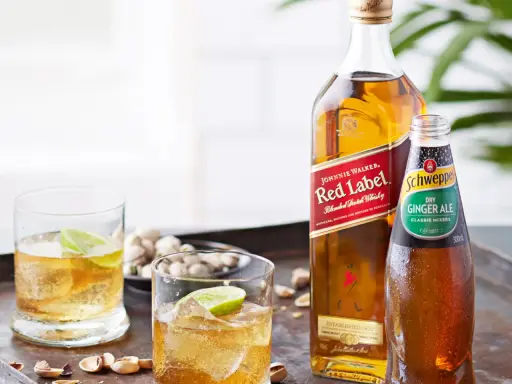 Butelka Johnnie Walker Red Label, butelka Schweppes Ginger Ale i dwa drinki z lodem i limonką.