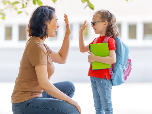 Madre y hija se dan un choque de manos, un momento de crianza positiva antes de ir a la escuela.