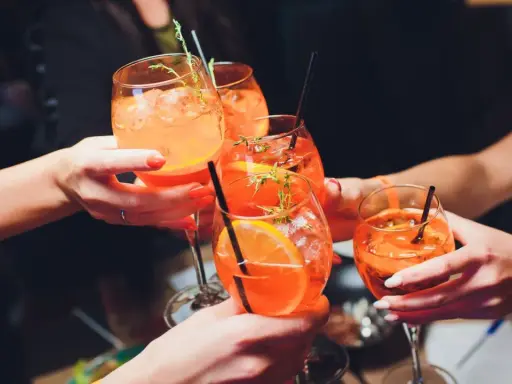 Hände stoßen mit Aperol Spritz an. So einfach wie man ihn macht, so erfrischend ist er!