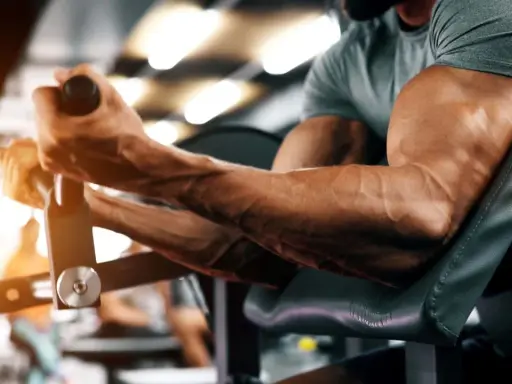 Ein Mann trainiert seinen Bizeps-Muskel an einem Gerät im Fitnessstudio. Die Adern treten deutlich hervor.