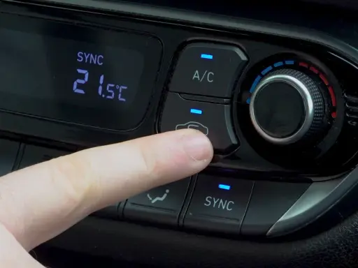 Dedo presionando el botón recirculacion aire del climatizador del coche.