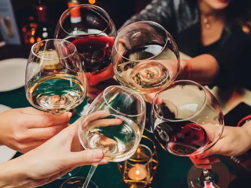 Hände heben Gläser mit Weiß- und Rotwein zum Anstoßen. Die ideale trinktemperatur für den Wein wird genossen.