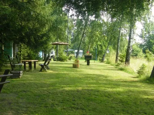 Zielony teren z drewnianymi ławkami i stołem, idealne miejsce na odpoczynek w pobliżu miasta nad Jeziorakiem.