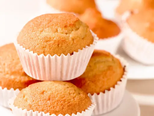 Ein Stapel goldbrauner, veganer Muffins in weißen Papierförmchen. Sie sehen köstlich und frisch gebacken aus.