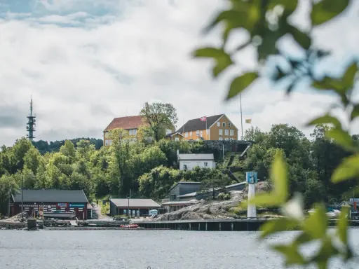 Widok na wybrzeże w Kristiansand, Norwegia. Żółte budynki na wzgórzu, czerwony klub kajakowy i wieża telekomunikacyjna.