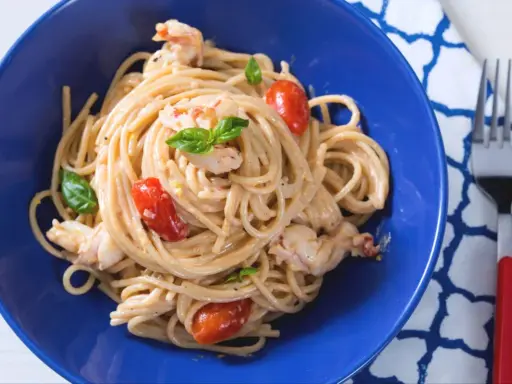 Un plat de pâtes aux crevettes, tomates cerises et basilic, servi dans un bol bleu vif. Un délice !