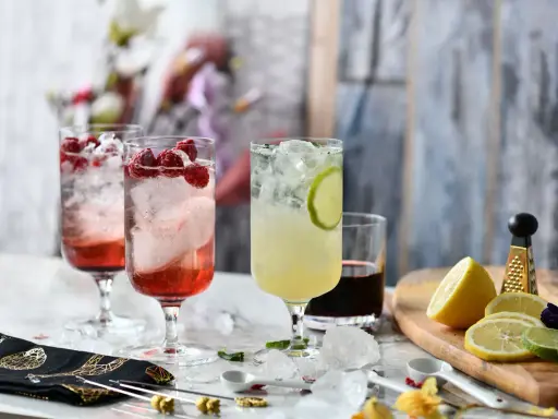 Orzeźwiające drinki na lato: malinowy z malinami i limonkowy z plasterkiem limonki, ozdobione lodem i miętą.