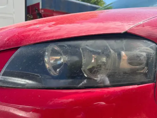 Faros sucios de coche rojo. El faro izquierdo muestra un anillo de luz, el derecho está rayado. La luz marcha atrás obligatoria es esencial para la seguridad.