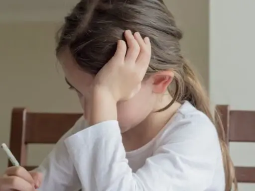 Dziewczynka z klasy 3 pisze dyktando, opierając głowę na dłoni.