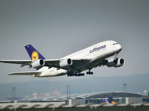 Samolot pasażerski Lufthansa z wysuniętym podwoziem startuje na tle lotniska.