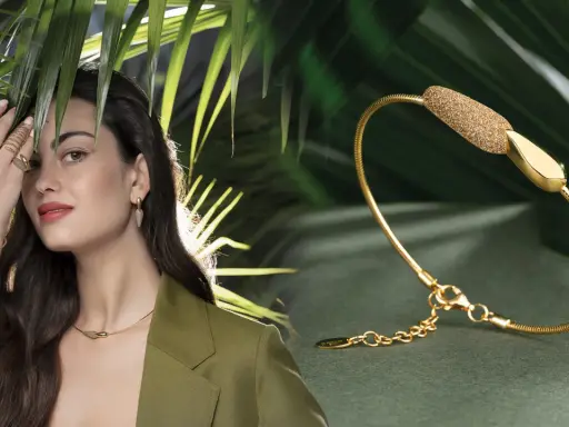 Modella con gioielli Pesavento, tra cui una collana, orecchini e anelli, su sfondo verde con foglie tropicali.