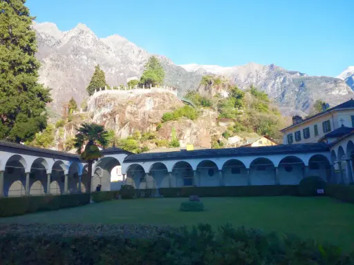 Un porticato ad archi domina un giardino curato, con montagne imponenti sullo sfondo. Un luogo ideale per scoprire cosa vedere a Chiavenna.