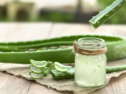 Goutte de gel d'aloe vera tombant dans un verre, prêt à être bu. Des tranches d'aloe vera sont disposées à côté.