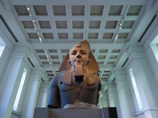 A colossal bust of an ancient Egyptian pharaoh, one of the museum's famous sculptures, stands majestically under a grand, coffered ceiling.