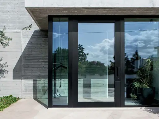 Puerta de entrada moderna con grandes ventanales de cristal, mostrando diferentes tipos de cristales para puertas exteriores que reflejan el cielo y la vegetación.