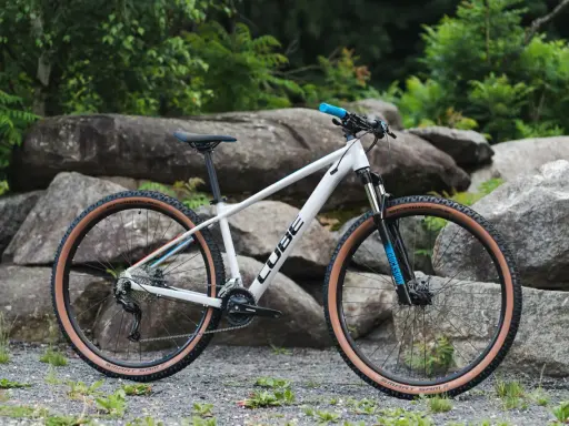 Biały rower Cube z brązowymi oponami, idealny jako rower na długie trasy. Wyposażony w amortyzator RockShox i napęd Shimano.