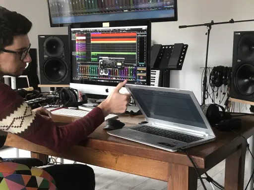 Un jeune sound engineer travaille dans son studio, entouré de matériel audio, d'écrans et d'un clavier.