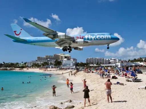 Samolot Airfly.com przelatuje nisko nad plażą pełną turystów, którzy obserwują jego lądowanie.