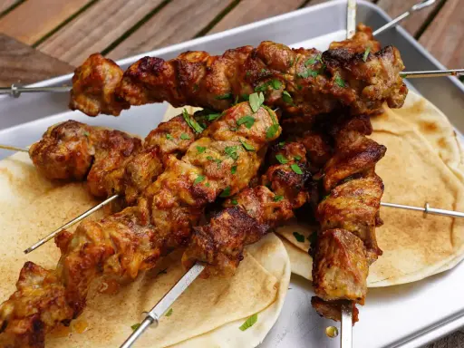 Saftige Schaschlik-Spieße, perfekt gegrillt, liegen auf Fladenbrot. Ein Genuss, der an ein gemütliches Essen im Dutch Oven erinnert.