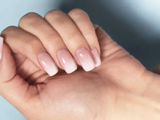 Dłoń z paznokciami w stylu francuski manicure, z delikatnym ombre od różu do bieli.