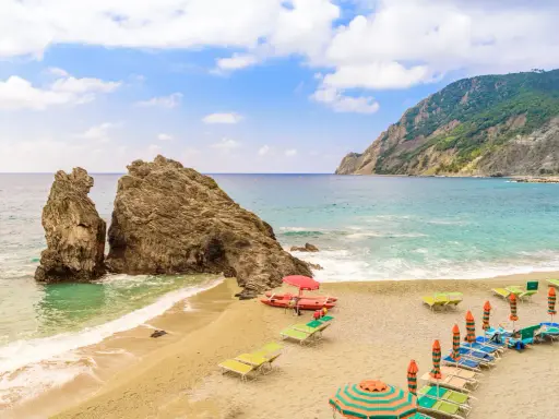Spiagge sabbia Liguria: scogli imponenti, mare turchese e lettini pronti per il relax.