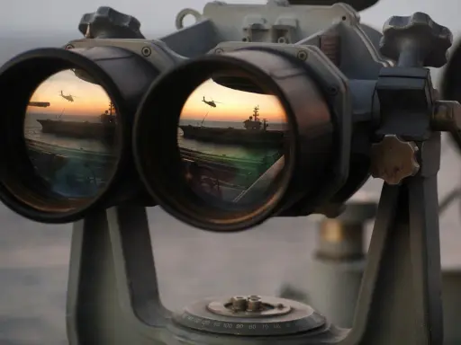 Fernglas-Werte: Ein Flugzeugträger und ein Hubschrauber spiegeln sich im Okular eines Fernglases bei Sonnenuntergang.