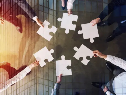 Manos unidas colocando piezas de rompecabezas, un símbolo de inteligencia colaborativa y trabajo en equipo para lograr un objetivo común.