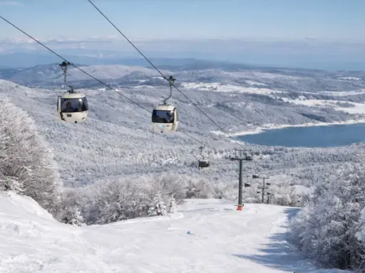 Funivia su montagne innevate, un lago azzurro sullo sfondo. Scopri dove sciare in Calabria per un'esperienza indimenticabile.