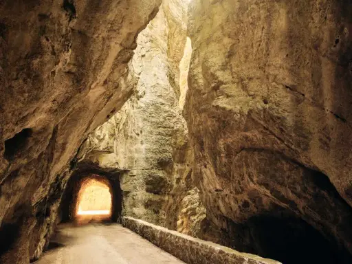 La strada della forra si snoda tra imponenti pareti rocciose, con un tunnel che si apre verso una luce accecante.